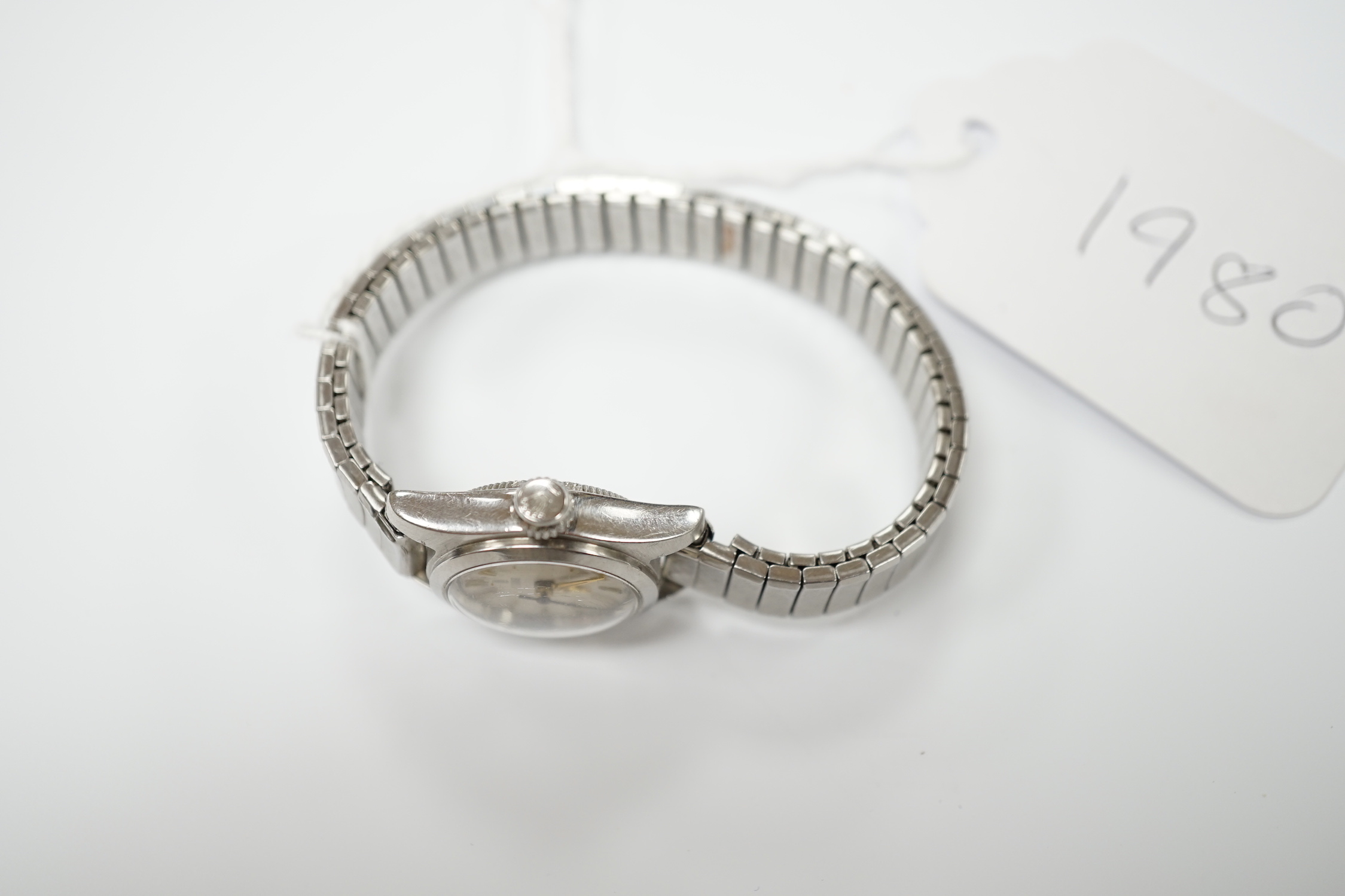 A lady's stainless steel Tudor manual wind wrist watch, with baton numerals, on an associated flexible bracelet.